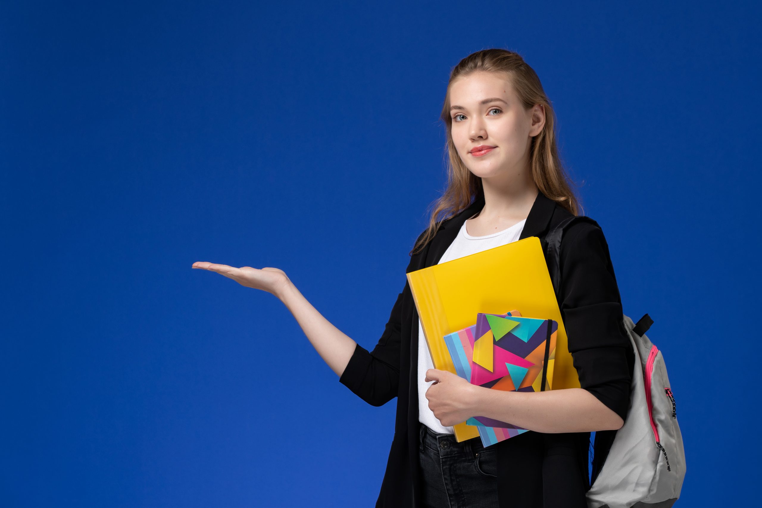 front-view-female-student-white-shirt-black-jacket-wearing-backpack-holding-files-with-copybooks-blue-wall-college-university-lessons-scaled.jpg